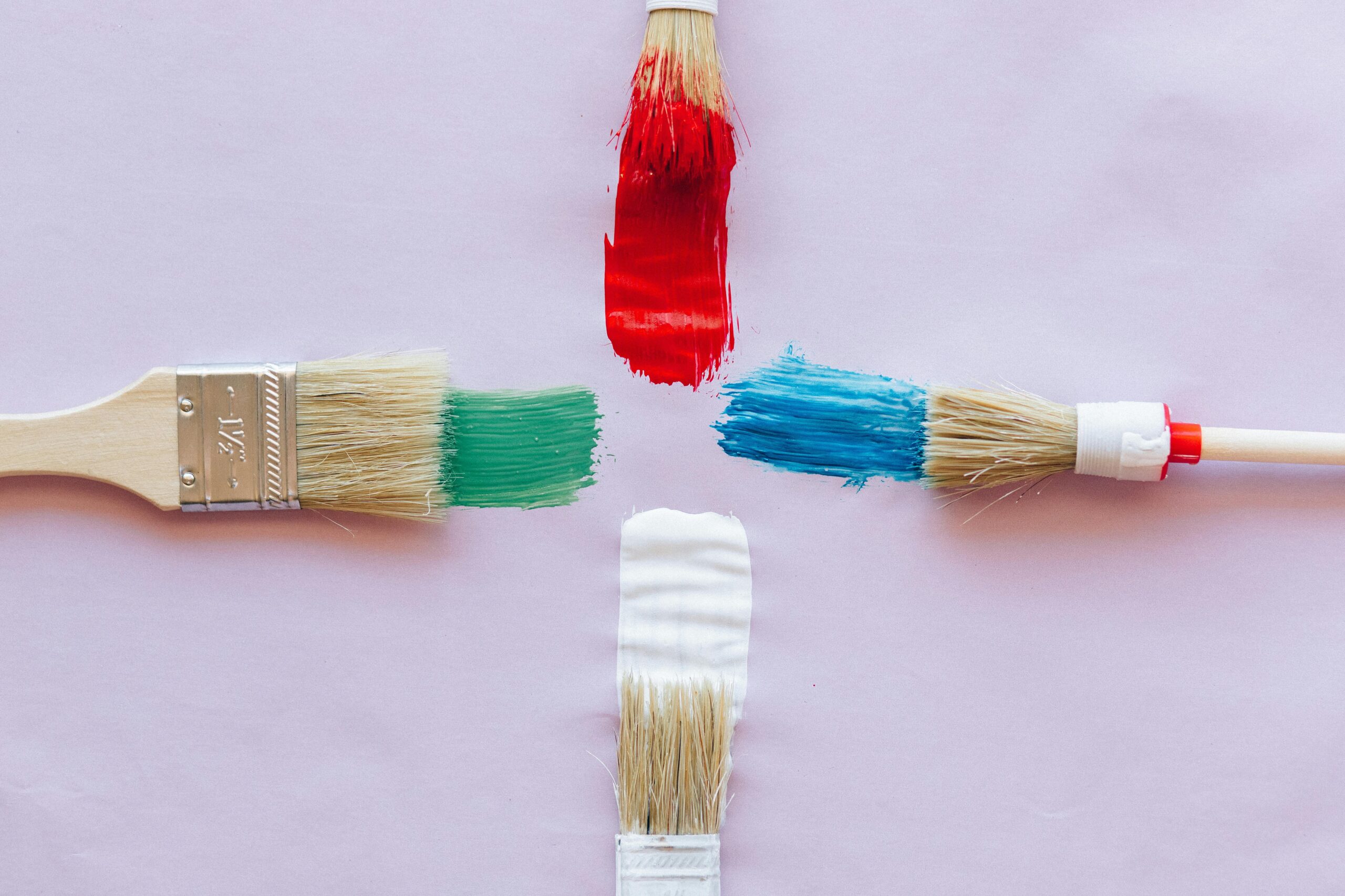 Four paint brushes with vibrant red, green, blue, and white strokes on pastel backdrop.